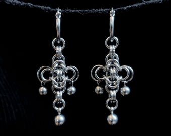 May include: A pair of silver-toned chainmaille earrings featuring a complex woven pattern of interlocking metal rings. Each earring is suspended from a circular hoop and terminates in a small, smooth spherical bead at the bottom and sides.