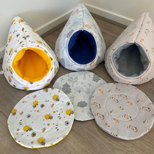 Peut inclure: Trois lits pour animaux en forme de goutte d'eau avec des coussins circulaires assortis. Un lit présente un tissu blanc avec des abeilles jaunes et un intérieur jaune vif. Un autre a un imprimé forêt bleu clair avec un intérieur bleu foncé. Le troisième a un imprimé animal rose clair avec un intérieur gris.