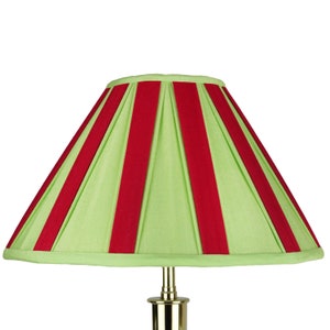 May include: A green lampshade with red vertical stripes. The lampshade is pleated and has a rounded top.