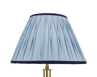 May include: A light blue lampshade with a navy blue trim. The lampshade is pleated and has a rounded shape.