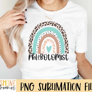 K&ouml;nnte beinhalten: Ein wei&szlig;es T-Shirt mit einem Regenbogen-Design mit einem Herzen und dem Text "Phlebotomist". Der Regenbogen besteht aus Braun, Pfirsich, Hellblau und Leopardenmuster.