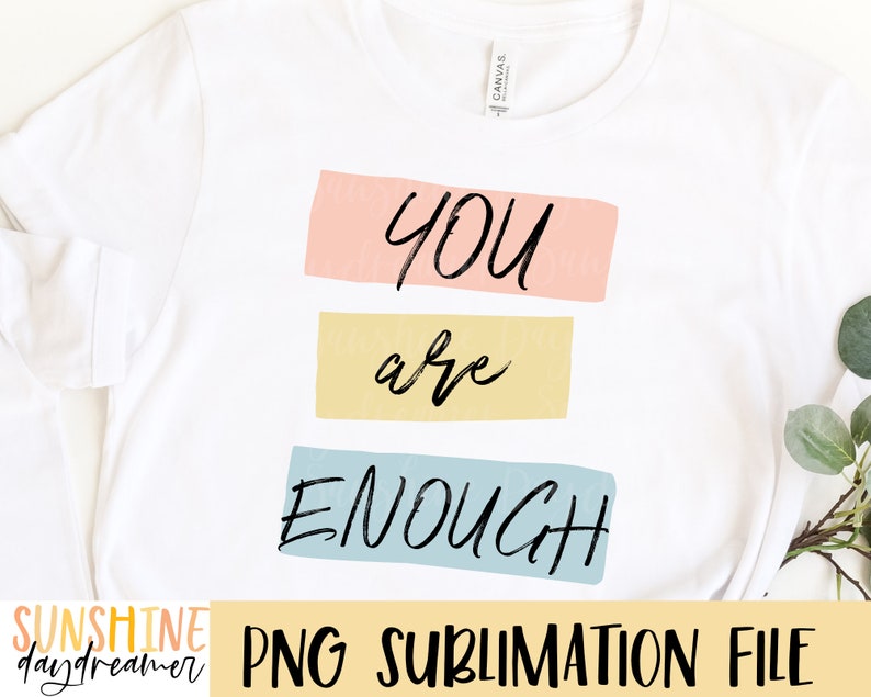May include: A white t-shirt with the text "YOU are ENOUGH" in black lettering on a colorful background. The text is in a handwritten style.