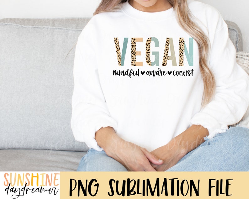 May include: White sweatshirt with the word "VEGAN" in blue and brown leopard print letters. The text "mindful aware coexist" is written below the word "VEGAN" in black.