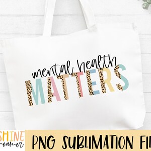 May include: A white tote bag with the text "mental health matters" in black script. The word "matters" is in colorful letters with a leopard print pattern.