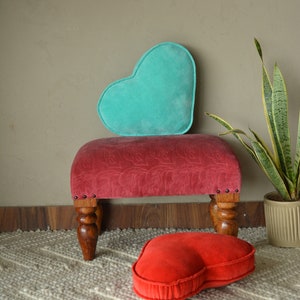 Pode incluir: Uma almofada de veludo turquesa em forma de cora&ccedil;&atilde;o repousa sobre um pufe de veludo vermelho com pernas de madeira entalhada. Uma segunda almofada em forma de cora&ccedil;&atilde;o, menor, em veludo vermelho est&aacute; no ch&atilde;o.