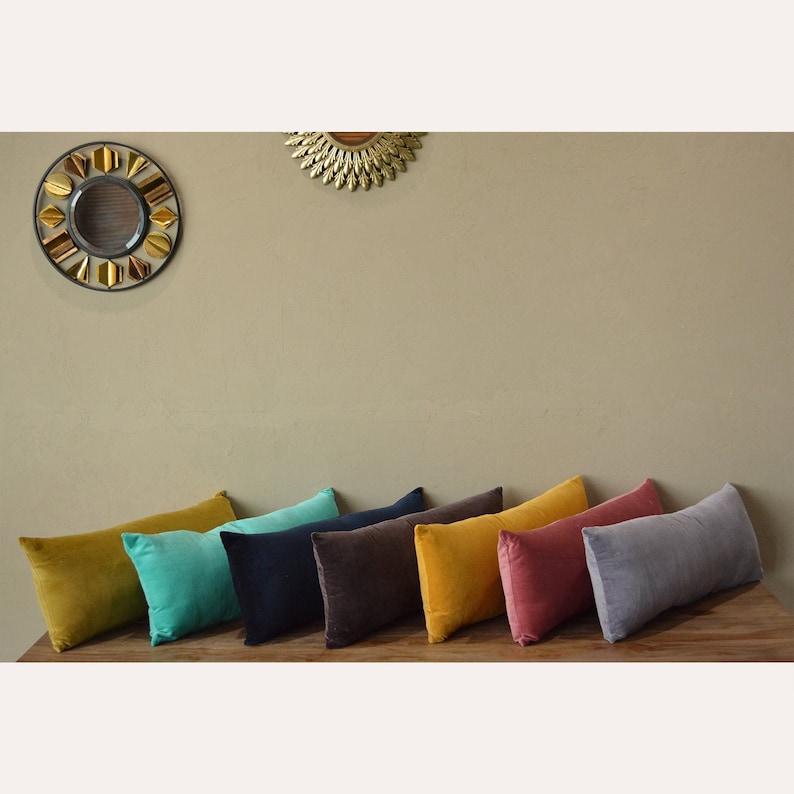 May include: A selection of rectangular cushions in shades of mustard, teal, navy, brown, and grey, displayed on a wooden surface. The cushions are arranged against a wall with two decorative mirrors.