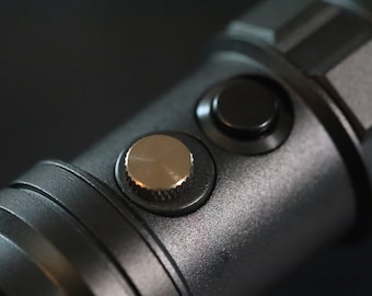 May include: Close-up of a black camera lens with a silver knob and a black button.