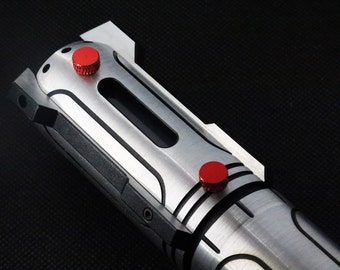 May include: A silver lightsaber hilt with black accents and two red buttons. The hilt has a textured surface and a cylindrical shape.