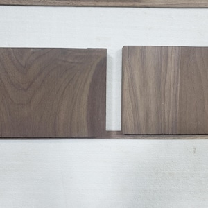 May include: Two rectangular wooden blocks with a dark brown grain pattern. The wood has a natural, unfinished appearance. The blocks are displayed against a white background, showcasing the wood's texture and color.