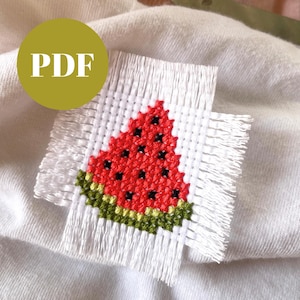 May include: A cross-stitch watermelon design on white fabric with a fringed edge. The watermelon is red with black seeds and a green rind. A yellow circle with the letters "PDF" is in the upper left corner.