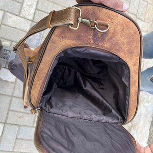 K&ouml;nnte beinhalten: Eine hellbraune Reisetasche aus Leder mit abgenutzter Textur und einer gro&szlig;en Rei&szlig;verschluss&ouml;ffnung, die ein dunkelbraunes Stoffinnenfutter freigibt. Die Tasche verf&uuml;gt &uuml;ber einen verstellbaren Schultergurt mit antikfarbenen Messingbeschl&auml;gen.