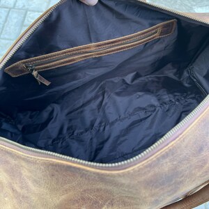 K&ouml;nnte beinhalten: Eine braune Reisetasche aus Leder mit dunkelbraunem Innenfutter. Die Tasche verf&uuml;gt &uuml;ber einen Rei&szlig;verschluss an der Oberseite und eine Innentasche mit Rei&szlig;verschluss und Lederbesatz. Das Au&szlig;enleder hat eine strukturierte, abgenutzte Optik.
