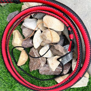 May include: A red and black braided bullwhip with a tassel. The whip is coiled on a bed of rocks.