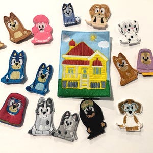May include: A collection of colorful felt finger puppets featuring cartoon dog characters and a yellow house with a red roof. The puppets are in various colors and designs, perfect for imaginative play.