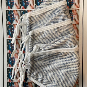 May include: A set of four white face masks with a blue and white chevron pattern. The masks have white elastic ear loops.