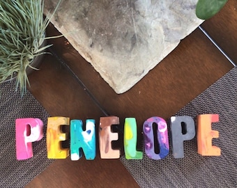 May include: The name Penelope spelled out in colorful crayon letters. Each letter is a different color and has a unique design.
