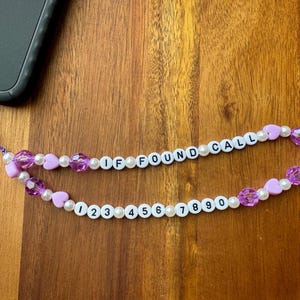 May include: A white and purple beaded phone charm with the words "IF FOUND CALL" and the numbers 1 through 9.