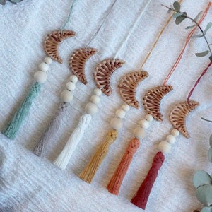 Könnte beinhalten: Sechs handgefertigte Makramee-Quasten-Ornamente mit Holzperlen und gewebten Halbmondformen. Die Quasten sind in den Farben Grün, Beige, Weiß, Gelb, Orange und Rot.