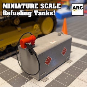 Puede incluir: Un tanque de combustible de plástico gris con una boquilla de combustible roja y negra. El tanque está etiquetado como "FUEL OIL" y está a escala 1/14 o 1/10. Es adecuado para usar en un diorama, en un escritorio o en un camión RC.