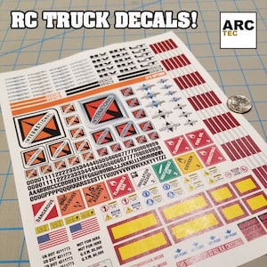 May include: A sheet of white sticker paper with red, black, and yellow decals for RC trucks. The decals feature the word "INTERNATIONAL" in a black and red logo, along with various warning signs and labels, including "Flammable", "Oxygen", "Combustible", "Dangerous", "Explosives", "Not for Hire", and "Fire Extinguisher Inside". The sheet also includes a red and white striped pattern, a red and white striped pattern, and a red and white striped pattern.