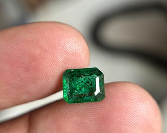 Könnte beinhalten: Ein rechteckiger Smaragd mit einem leuchtend grünen Farbton und sichtbaren inneren Einschlüssen. Der Stein weist einen Facettenschliff auf, der das Licht reflektiert und ein tiefes, gesättigtes Farbprofil in seiner gesamten Kristallstruktur zeigt.