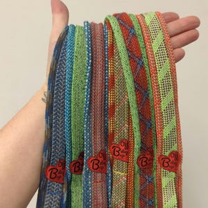 May include: A collection of colorful, woven, rope-like straps with red heart-shaped tags that say "Oh Belay Bags".