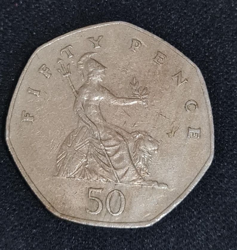 Puede incluir: Una moneda plateada de cincuenta peniques. La moneda presenta a Britannia sentada, sosteniendo un tridente y una rama de olivo, con un le&oacute;n a su lado. El n&uacute;mero 50 se muestra de forma destacada. La moneda es de forma octogonal.