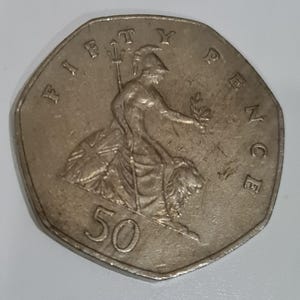 Puede incluir: Una moneda de cincuenta peniques de plata. La moneda presenta a Britannia sentada, sosteniendo un tridente y una rama de olivo. El borde de la moneda es heptagonal. El texto 'FIFTY PENCE' es visible.