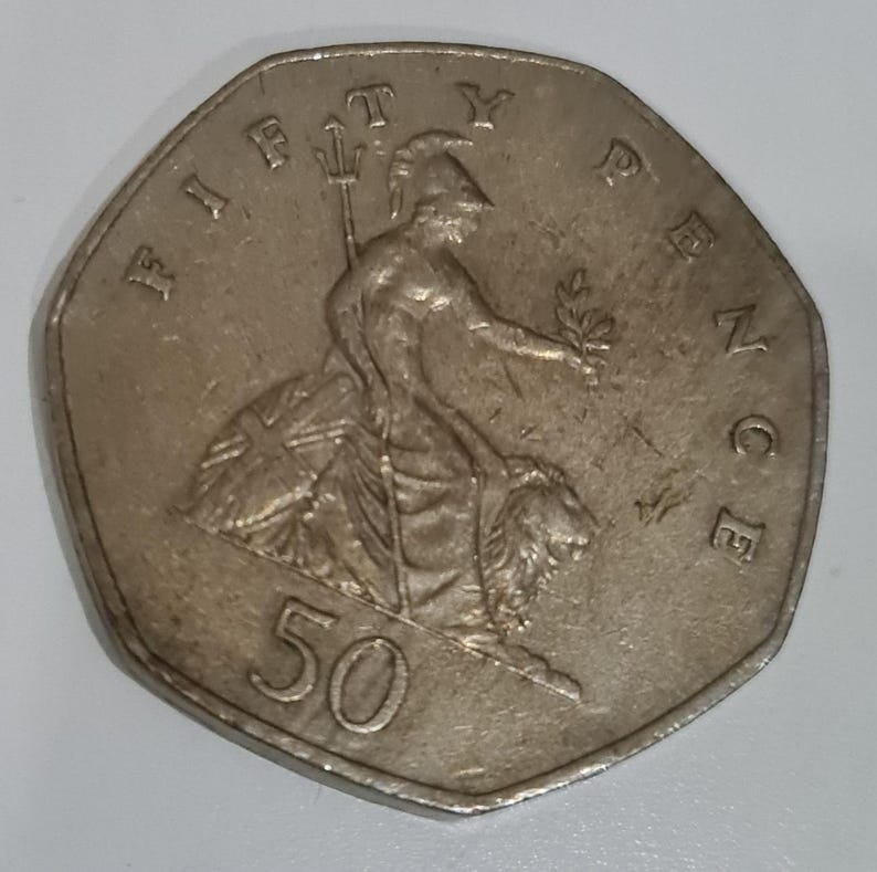 Puede incluir: Una moneda de cincuenta peniques de plata. La moneda presenta a Britannia sentada, sosteniendo un tridente y una rama de olivo. El borde de la moneda es heptagonal. El texto 'FIFTY PENCE' es visible.