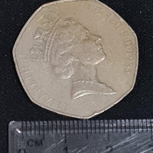 Puede incluir: Una moneda de cincuenta peniques de plata con el perfil de la reina Isabel II, con el a&ntilde;o 1983 visible. La moneda est&aacute; colocada junto a una regla con marcas de cent&iacute;metros.
