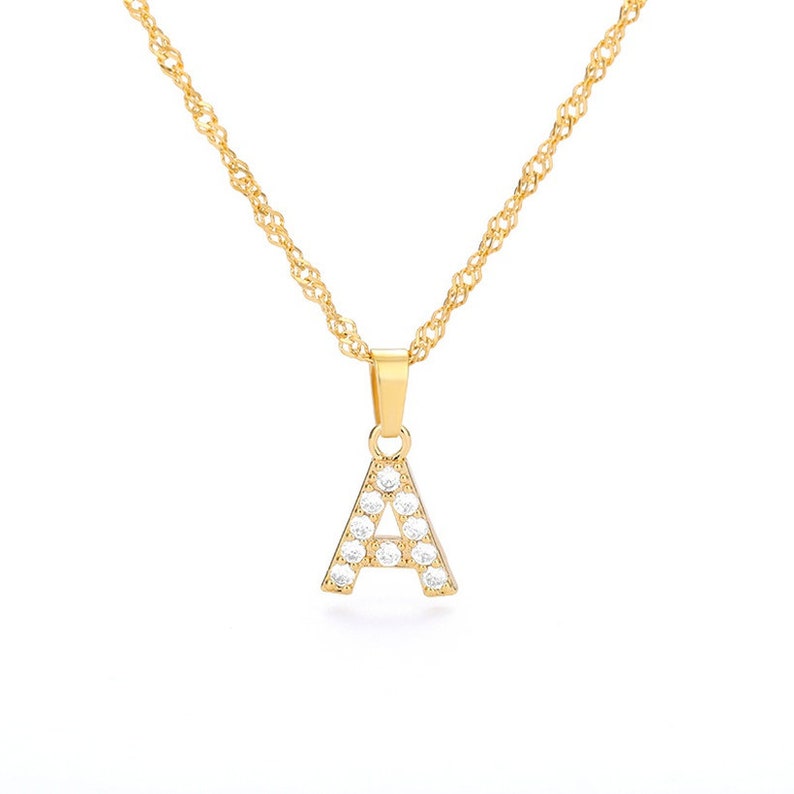 May include: A gold chain necklace with a pendant in the shape of the letter A. The pendant is encrusted with clear cubic zirconia stones.