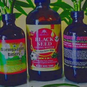 Puede incluir: Tres botellas de vidrio de líquido oscuro con etiquetas. Las botellas están etiquetadas como "Moringa Living Bitters", "Black Seed Living Bitter" y "Uroso Bitters". Las botellas están sobre una superficie verde.