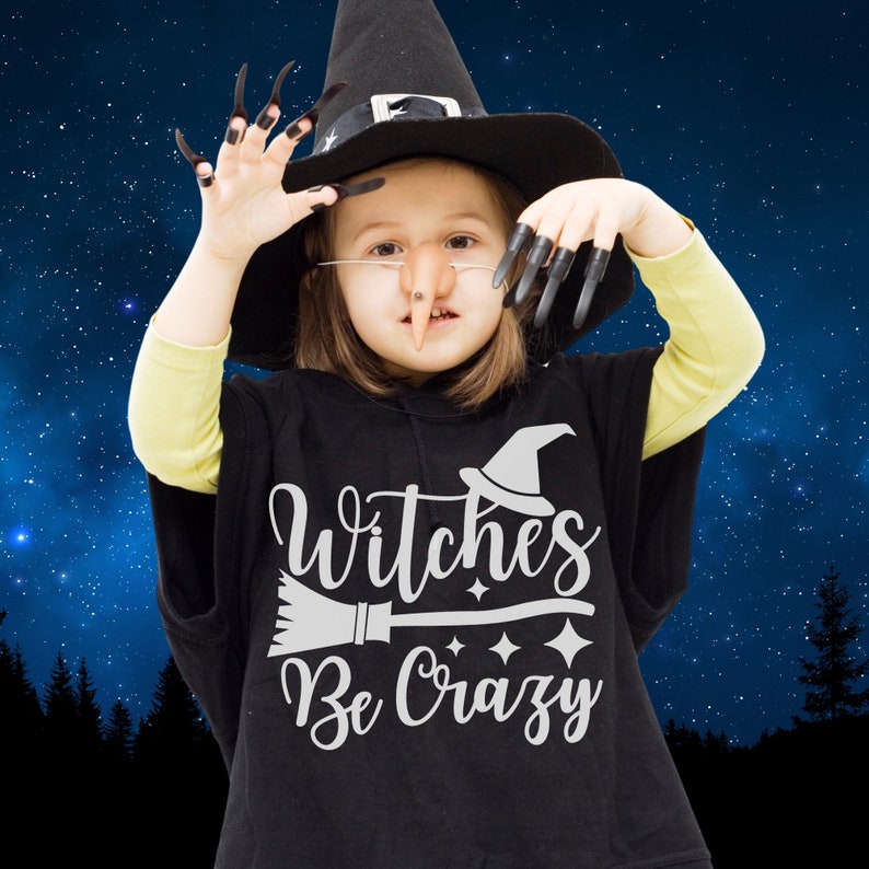 May include: A child dressed as a witch for Halloween, wearing a black witch's hat and a black shirt with the text "Witches Be Crazy" in white. The child is holding a broom and has a fake nose and witch's fingers.