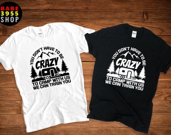May include: Two t-shirts with a camping theme. The white t-shirt has black text that reads "You don't have to be crazy to camp with us, we can train you". The black t-shirt has white text that reads "You don't have to be crazy to camp with us, we can train you". Both t-shirts have a graphic of a camper and trees.
