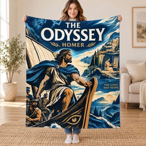May include: A rectangular throw blanket featuring a blue and cream illustration of The Odyssey by Homer. The design depicts a bearded figure in a blue cloak standing on a boat with a large eye motif, alongside text reading The Odyssey, Homer, and The Long Way Home.