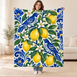 May include: A soft throw blanket featuring a vibrant pattern of bright yellow lemons, white citrus blossoms, and deep blue birds perched on leafy branches, all set against a white background with blue floral scrollwork accents.