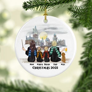 Może przedstawiać: Biała ceramiczna ozdoba świąteczna z rodzinną sceną i zamkiem w tle. Ozdoba zawiera tekst "CHRISTMAS 2025" i imiona. Rodzina ma na sobie szaliki i trzyma różdżkę i napój.