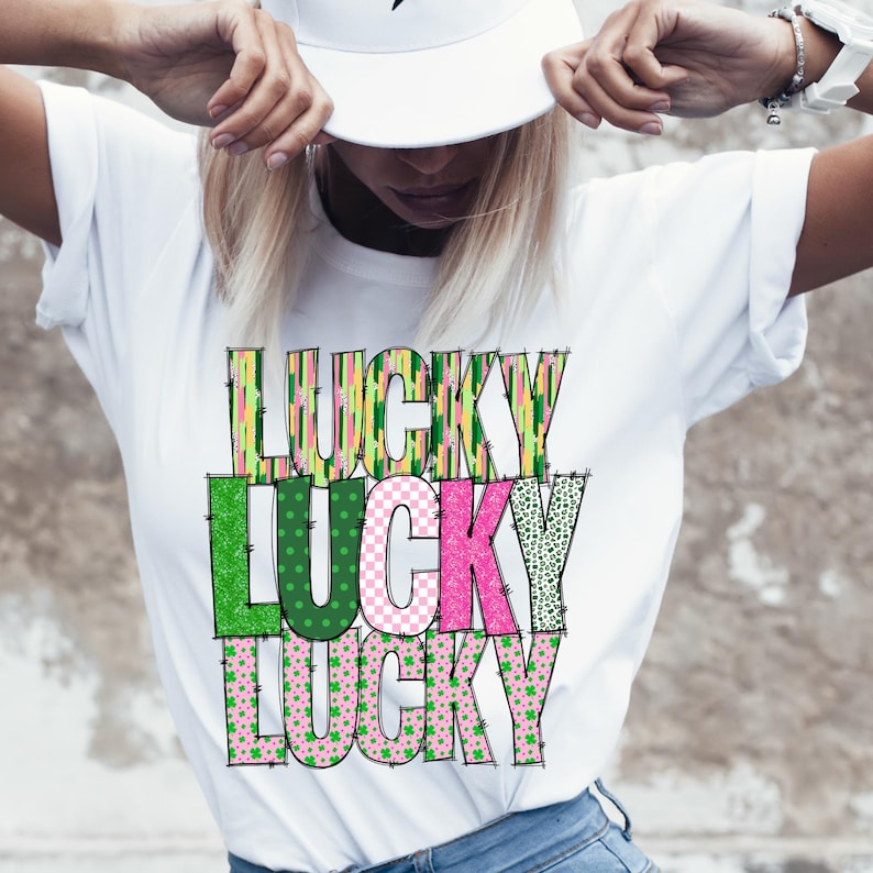 Pu&ograve; includere: Maglietta bianca con la parola "LUCKY" ripetuta tre volte in un design impilato. Ogni lettera &egrave; composta da diversi tessuti a motivi verdi, rosa e gialli.
