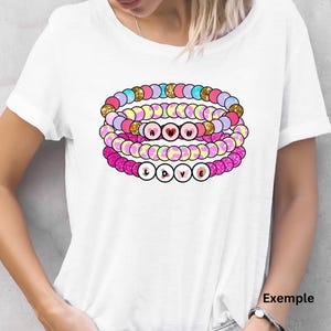 K&ouml;nnte beinhalten: Ein wei&szlig;es T-Shirt mit einem Stapel von vier bunten Perlenarmb&auml;ndern, die "LOVE" buchstabieren. Die Armb&auml;nder sind rosa, gelb, blau und lila mit Glitzerakzenten.