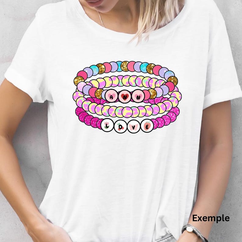 K&ouml;nnte beinhalten: Ein wei&szlig;es T-Shirt mit einem Stapel von vier bunten Perlenarmb&auml;ndern, die "LOVE" buchstabieren. Die Armb&auml;nder sind rosa, gelb, blau und lila mit Glitzerakzenten.