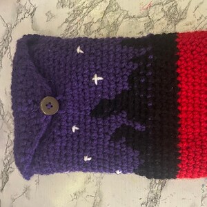 May include: A purple, black, and red crocheted phone case with a button closure and a star pattern.