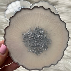 May include: Set of three white agate coasters with a silver glitter centre. The coasters have a scalloped edge and are perfect for protecting surfaces from scratches and spills.