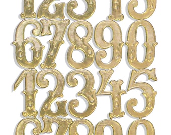 May include: A sheet of gold-coloured metal numbers, including digits 0-9, in a vintage, ornate font. The numbers are connected by thin metal strips. The numbers are arranged in rows and columns against a white background.