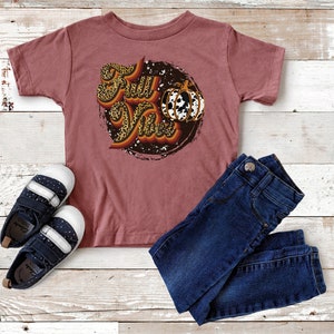 May include: A maroon short-sleeved t-shirt with a graphic of a pumpkin and the text "Fall Vibes" in a leopard print design.
