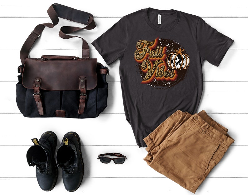 May include: A dark gray t-shirt with a graphic of a pumpkin and the text "Fall Ya'll" in a retro font. The graphic is surrounded by a leopard print pattern and a distressed circle.
