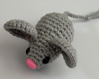 Può includere: Un giocattolo di topo in crochet grigio con il naso rosa e gli occhi neri. Il topo ha una coda lunga.