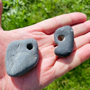 May include: Two gray stones with holes drilled through them. The stones are smooth and have a natural, weathered look.