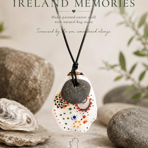 Peut inclure: Un collier composé d'un pendentif en coquille d'huître blanche peinte à la main avec des points colorés et une pierre naturelle percée, suspendu à un cordon noir. Le texte IRELAND MEMORIES, Hand-painted oyster shell with natural hag stone, Treasured by the sea, remembered always, et CRAFTED BY NATURE INSPIRED BY IRELAND est visible.