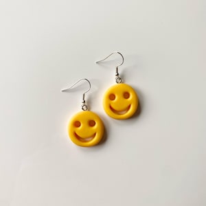 Peut inclure: Une paire de boucles d'oreilles jaunes en forme de smiley avec des crochets argentés.
