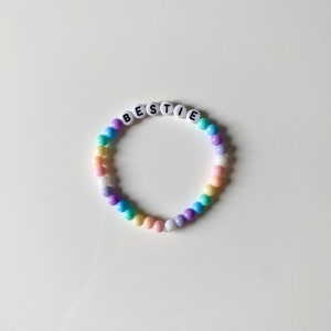 May include: A rainbow beaded bracelet with the word "BESTIE" spelled out in black letters on white beads.